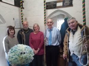 5 bellringers standing in a bellringing chamber with 3 bell ropes visible.